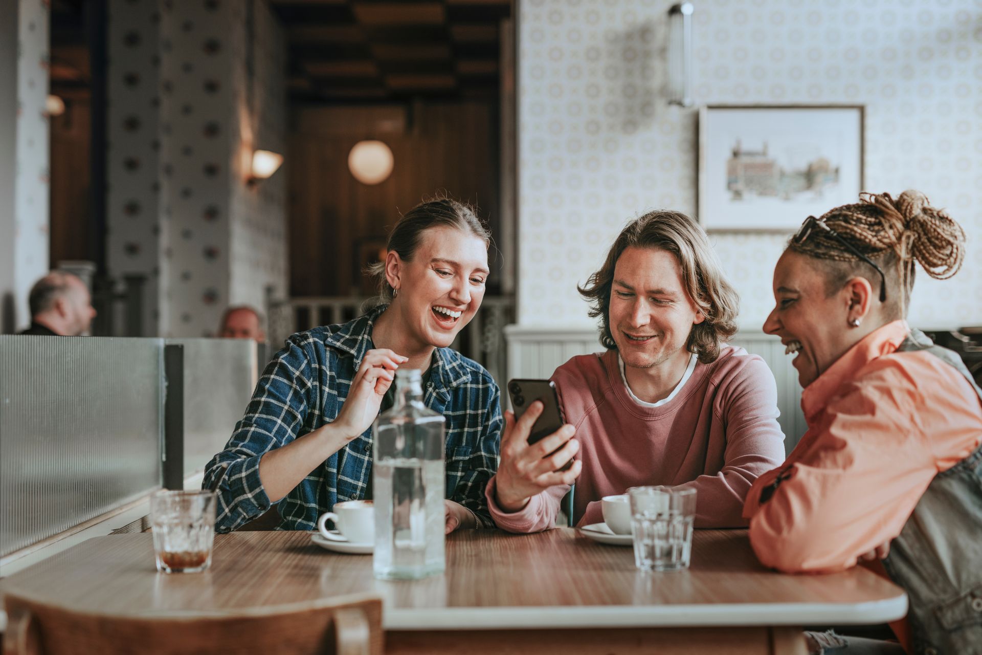 Three friends chatting and smiling at a café table with drinks and a water bottle.