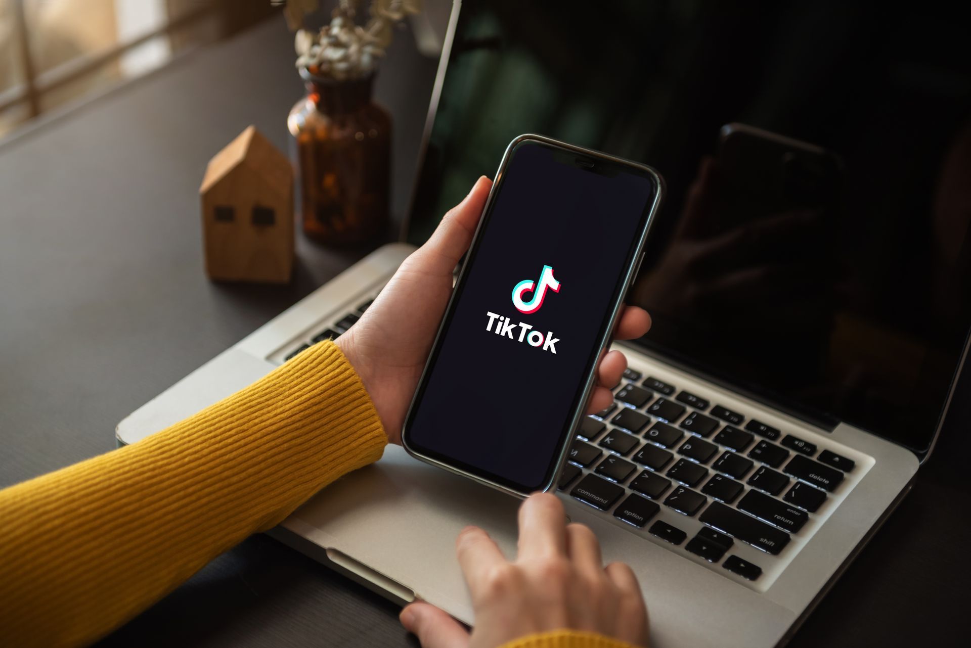 Hand holding a smartphone with the TikTok logo over a laptop keyboard