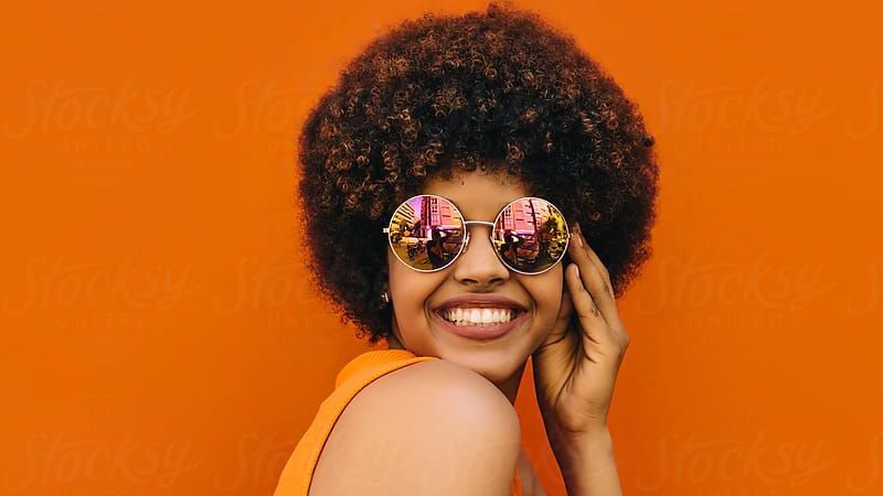 Smiling person in mirrored sunglasses against a bright orange background