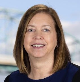 Smiling woman with shoulder-length brown hair in a navy top against a blurred office-like background, CPA, Accounting