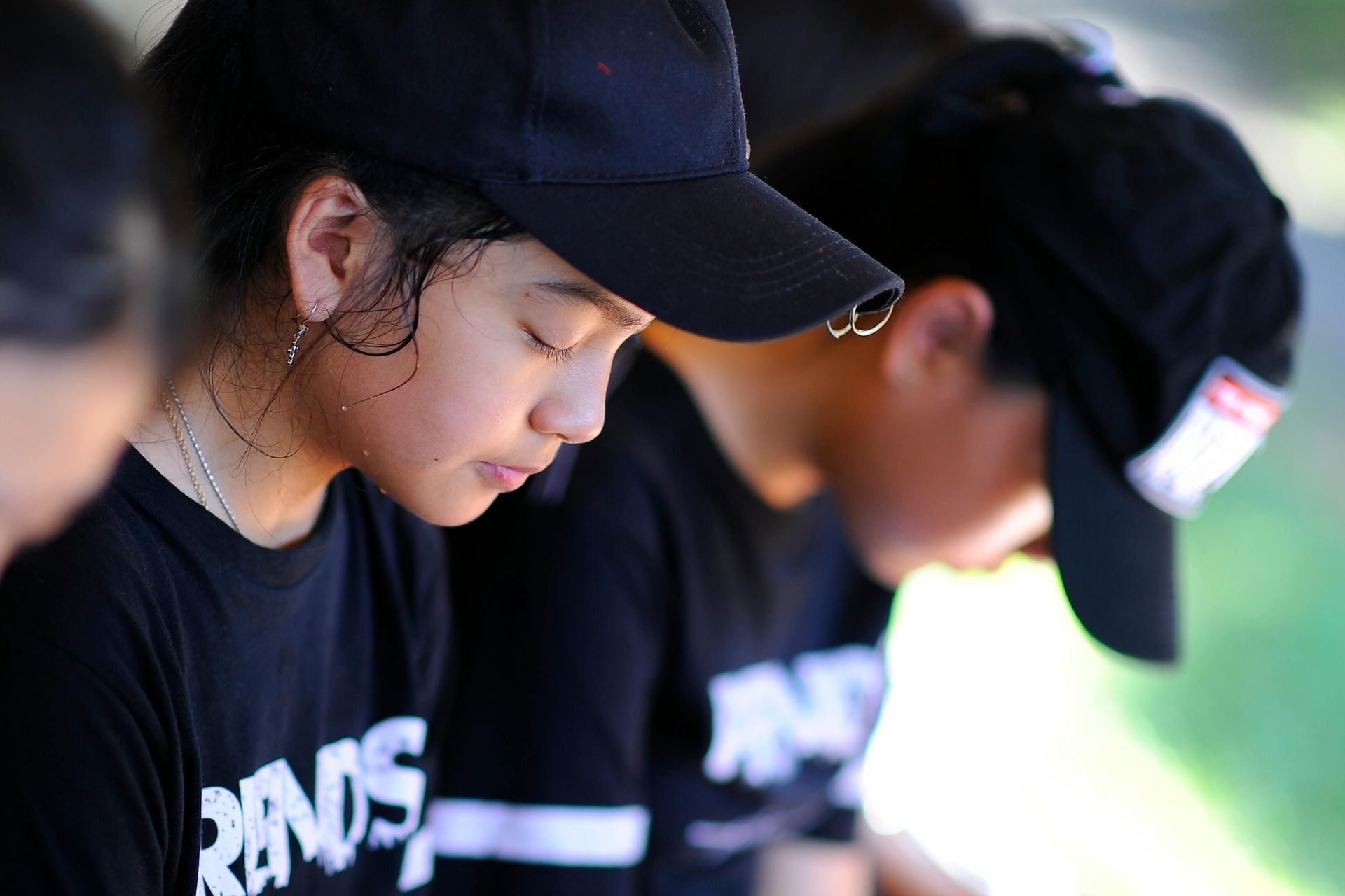 Two people in black caps and shirts lean forward outdoors, focused on an activity.