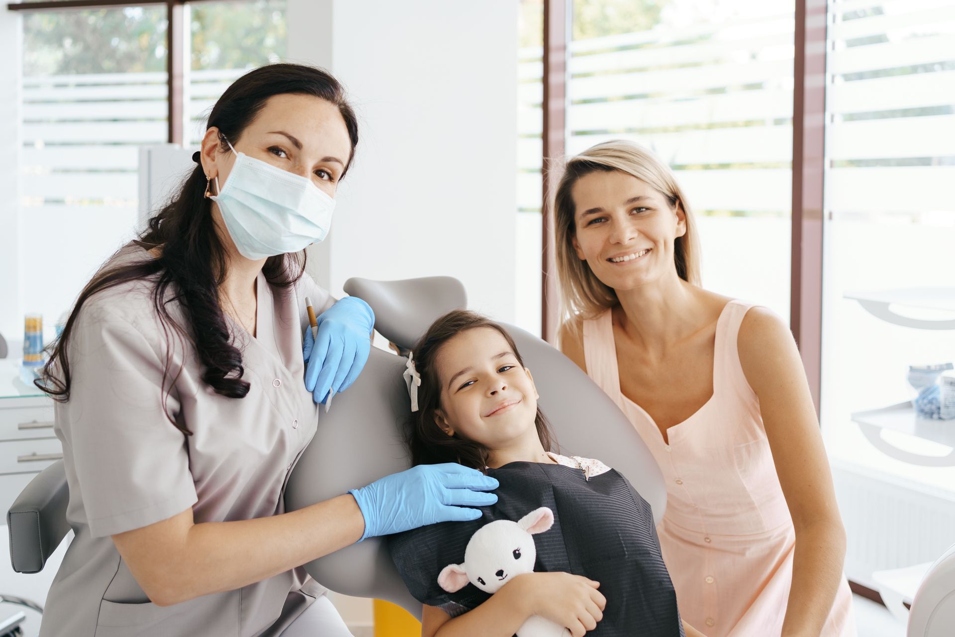 A woman is sitting next to a little girl in a dental chair.