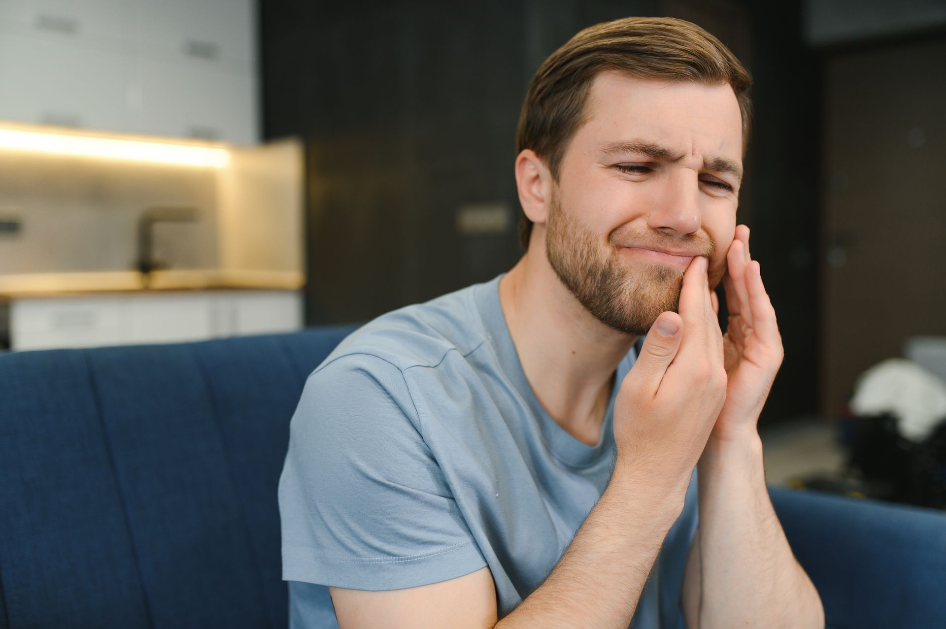 A man is sitting on a couch with a toothache.