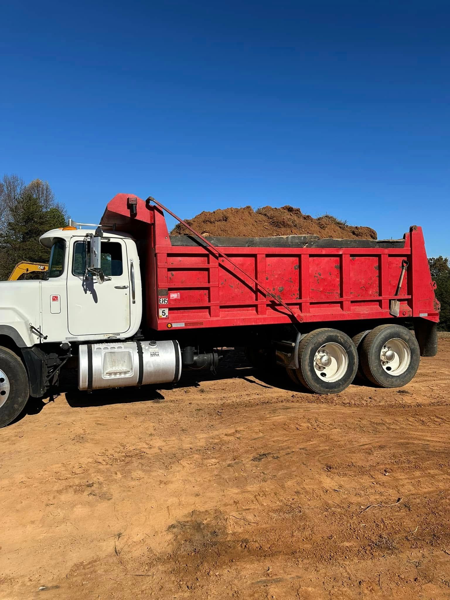 A white and red dump truck filled with dirt parked on a construction site under a clear blue sky.