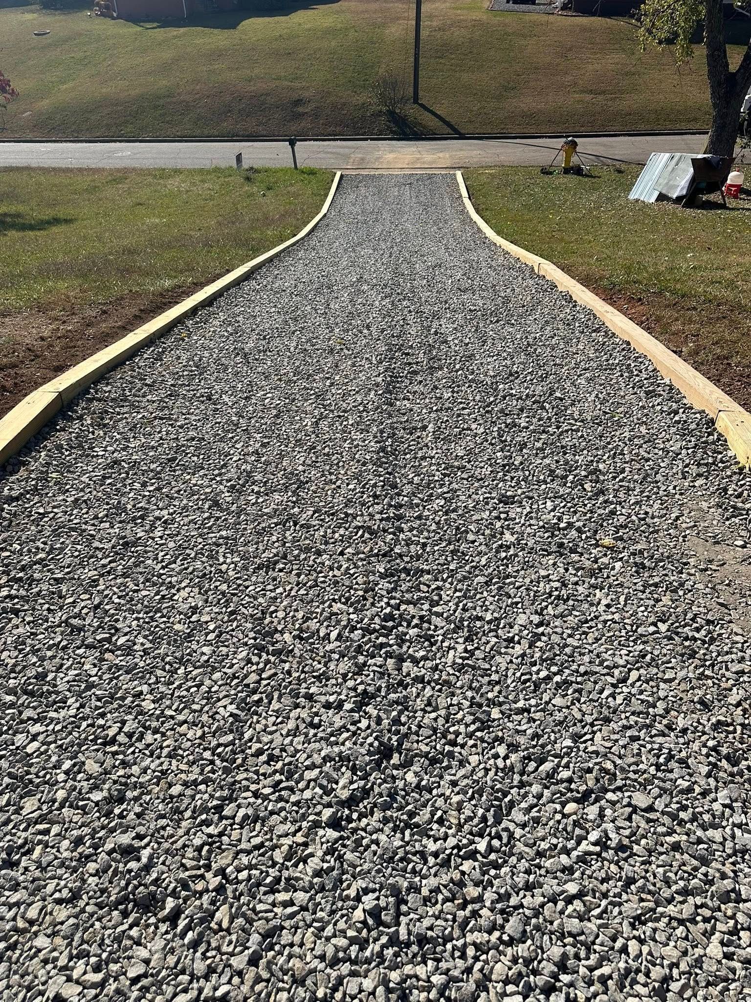 A gravel path with light wood edging leading toward a road on a sunny day.