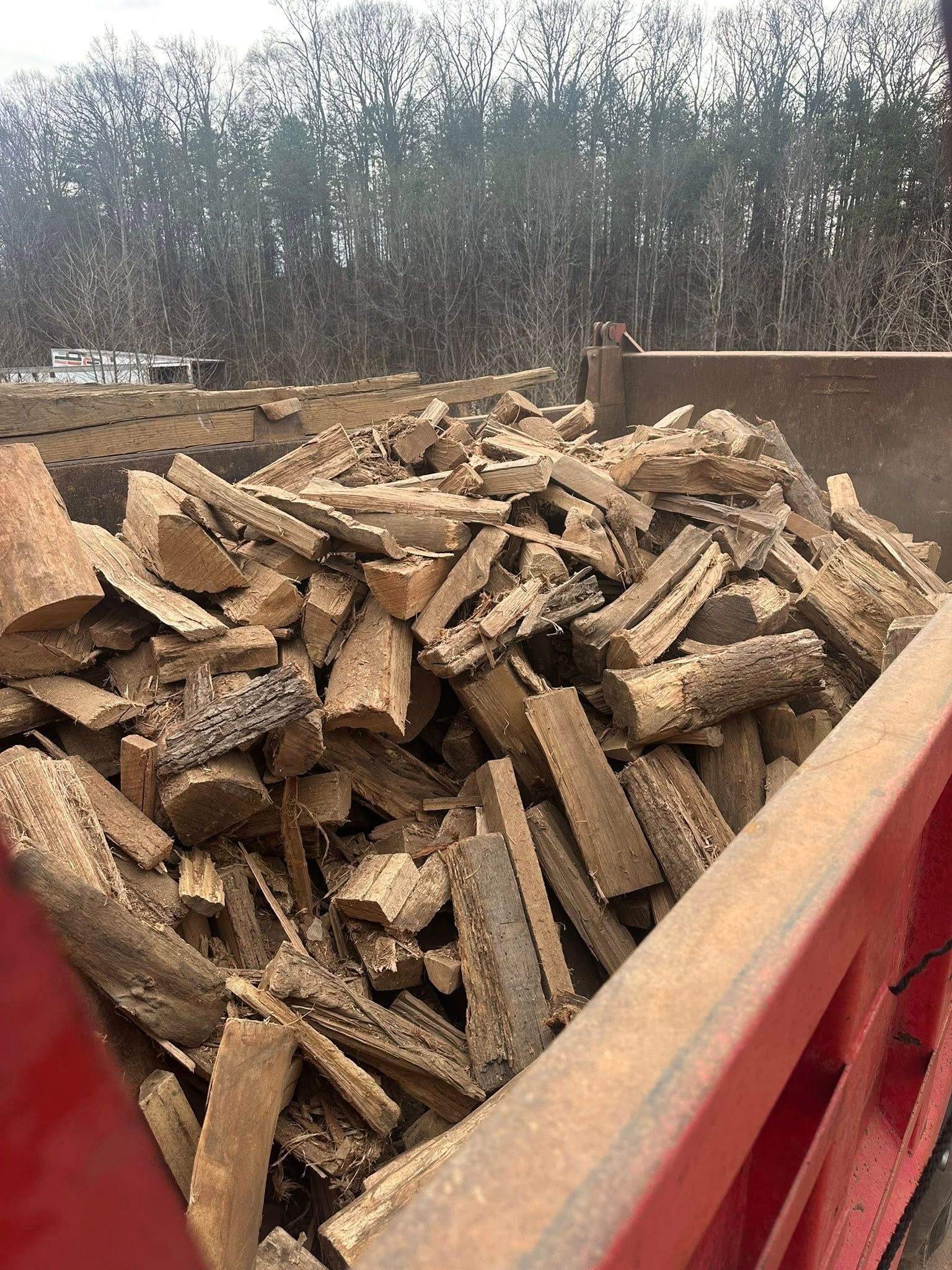 A large, overflowing metal dump truck bed filled with cut, split pieces of dry, light brown firewood.