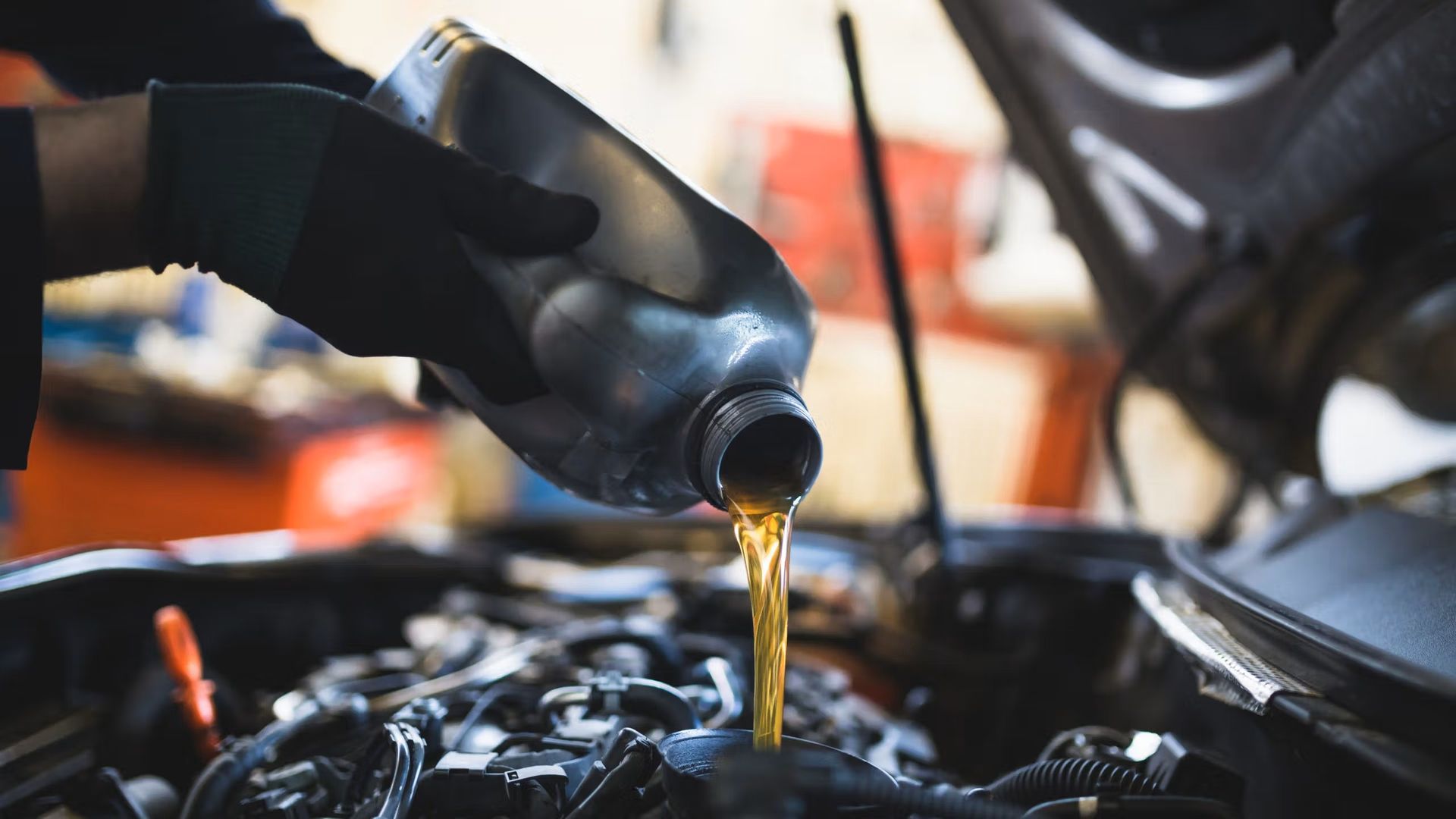 Fresh engine oil being poured into the filler neck under an open hood