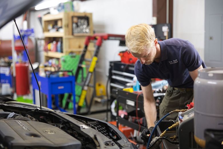 Mechanic working under an open car hood in a bright auto repair shop Mechanic working under an open car hood in a garage with tools and shelves in the background
