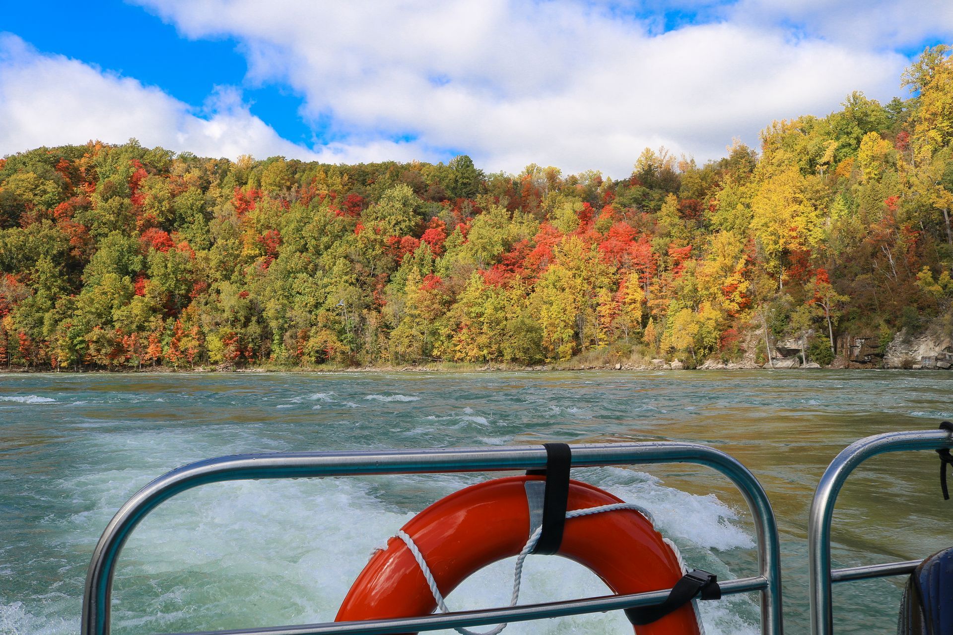 Autumn foliage lines the Niagara River Gorge, viewed from a jet boat on the water.