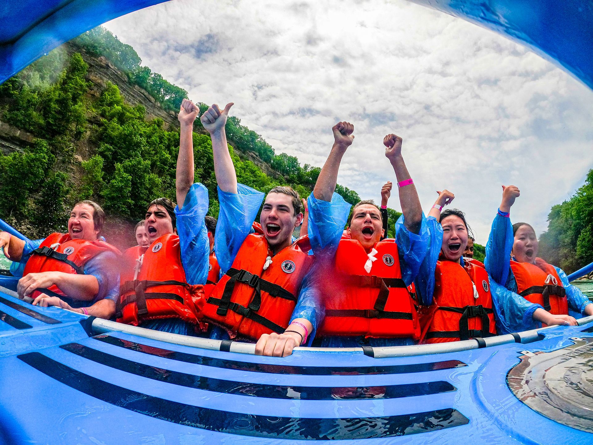 Whirlpool Jet Boat passengers cheer with their arms raised during a wet jet boat tour.