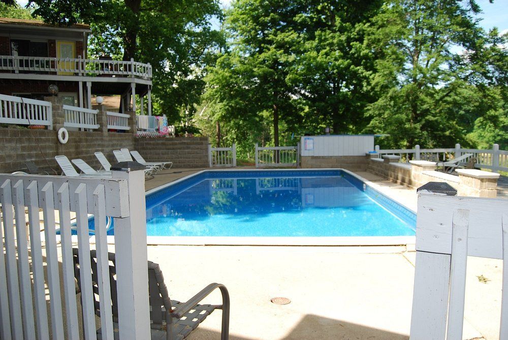Backyard swimming pool with white fence, patio chairs, and a house on a sunny day