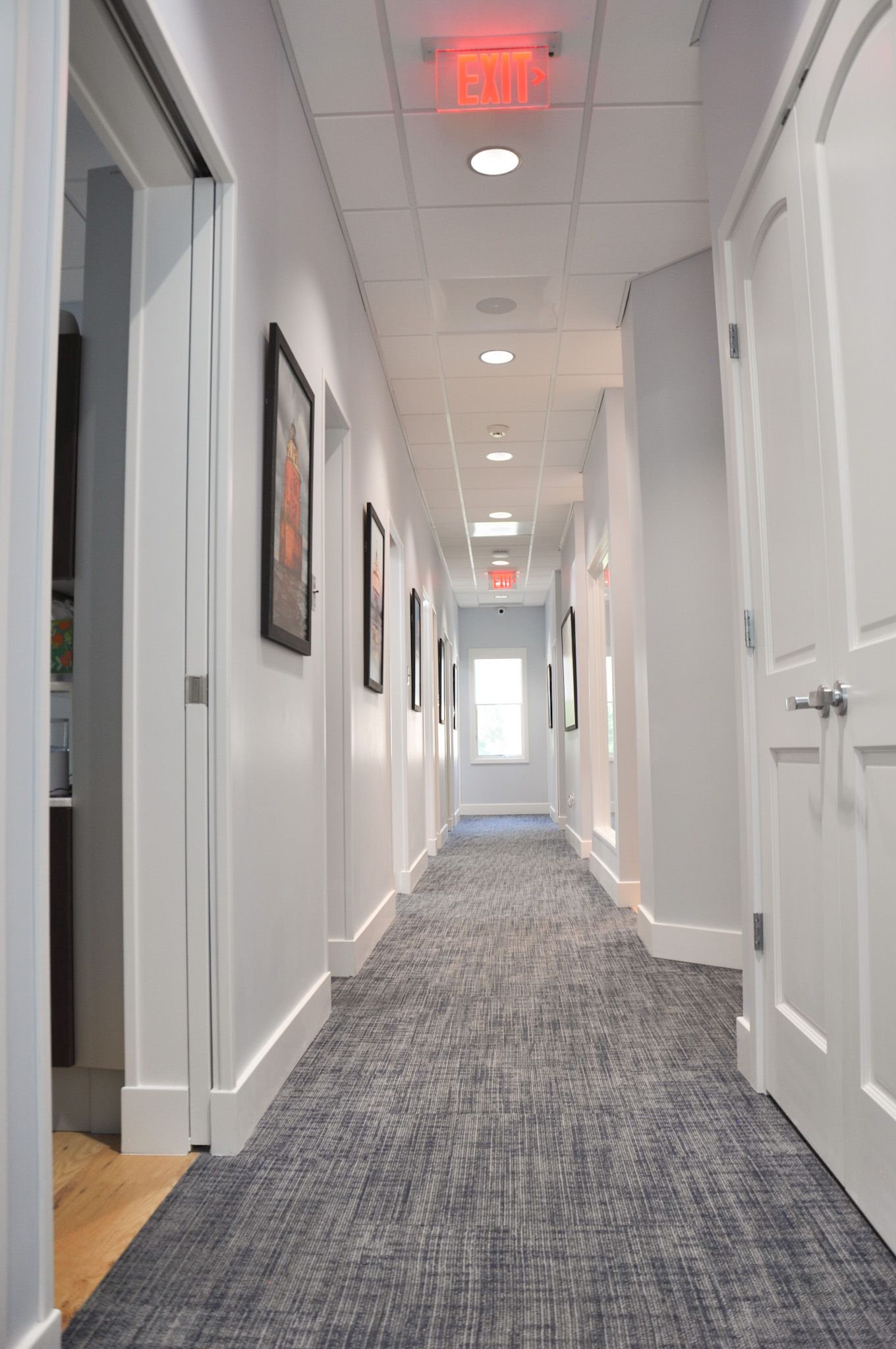 Narrow white hallway with doors, framed art, and patterned carpet.