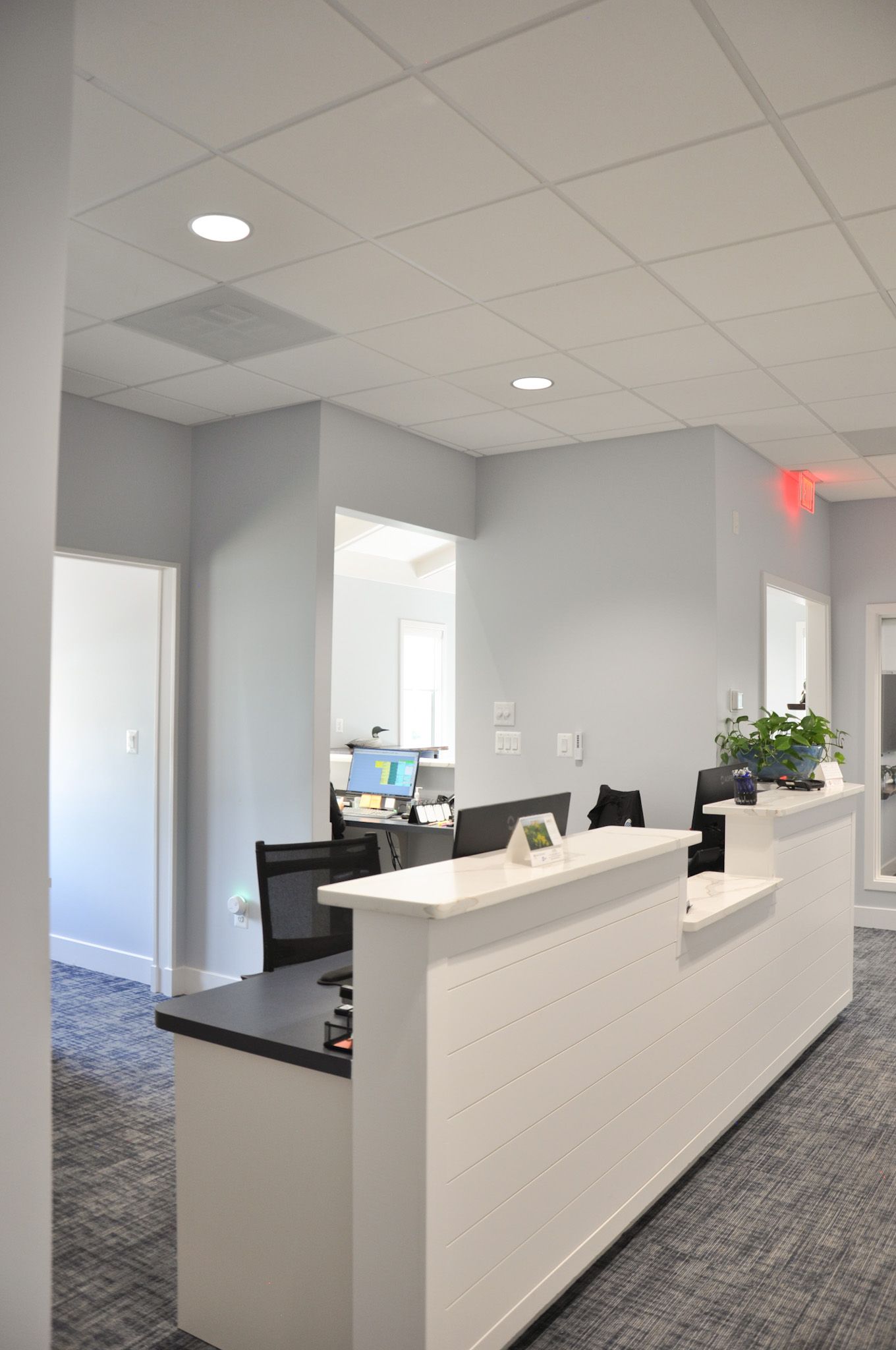 Modern office reception area with white desk, gray walls, and recessed lighting.