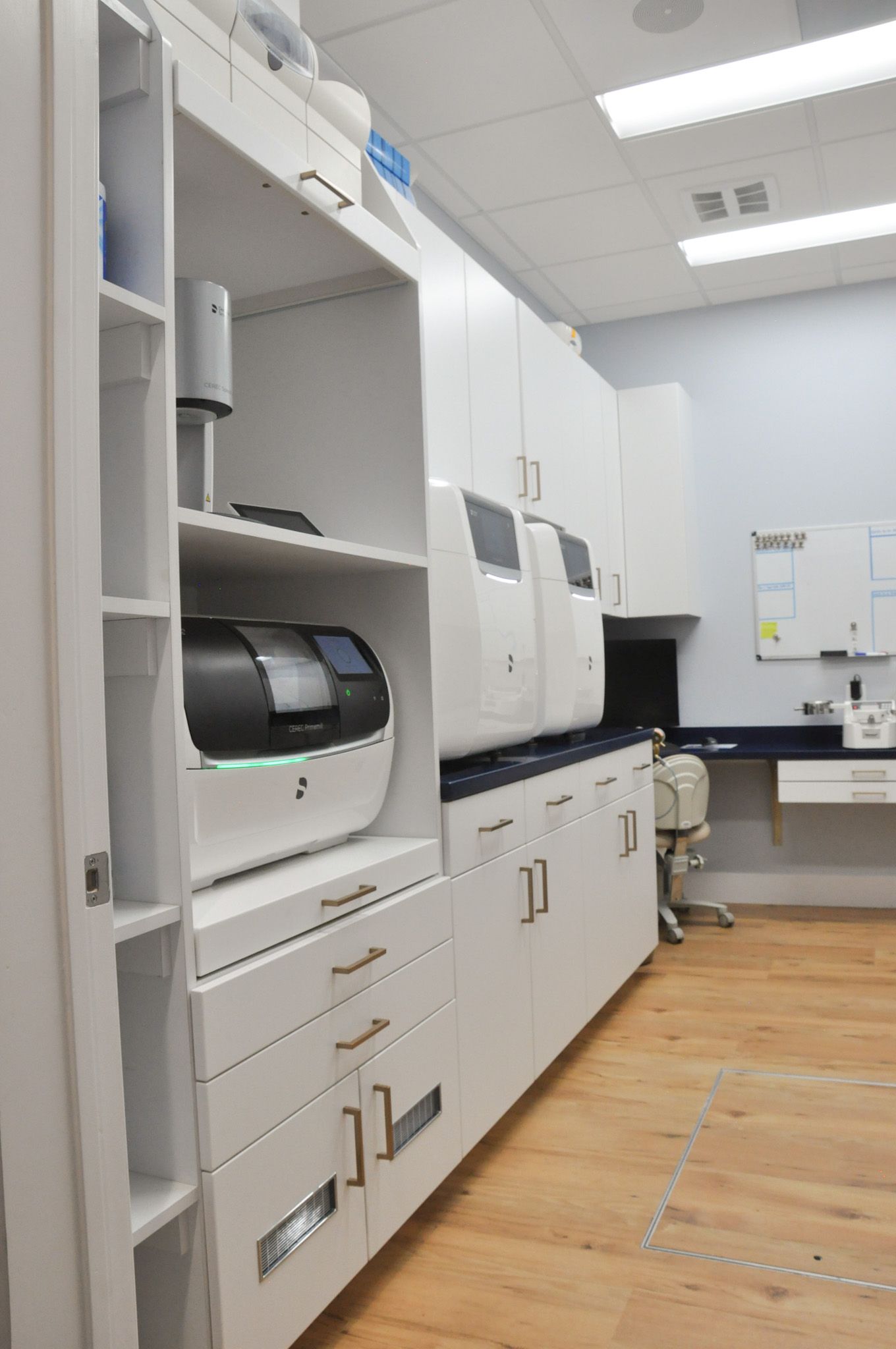 Dental lab with white cabinets, dental equipment, and wood flooring.