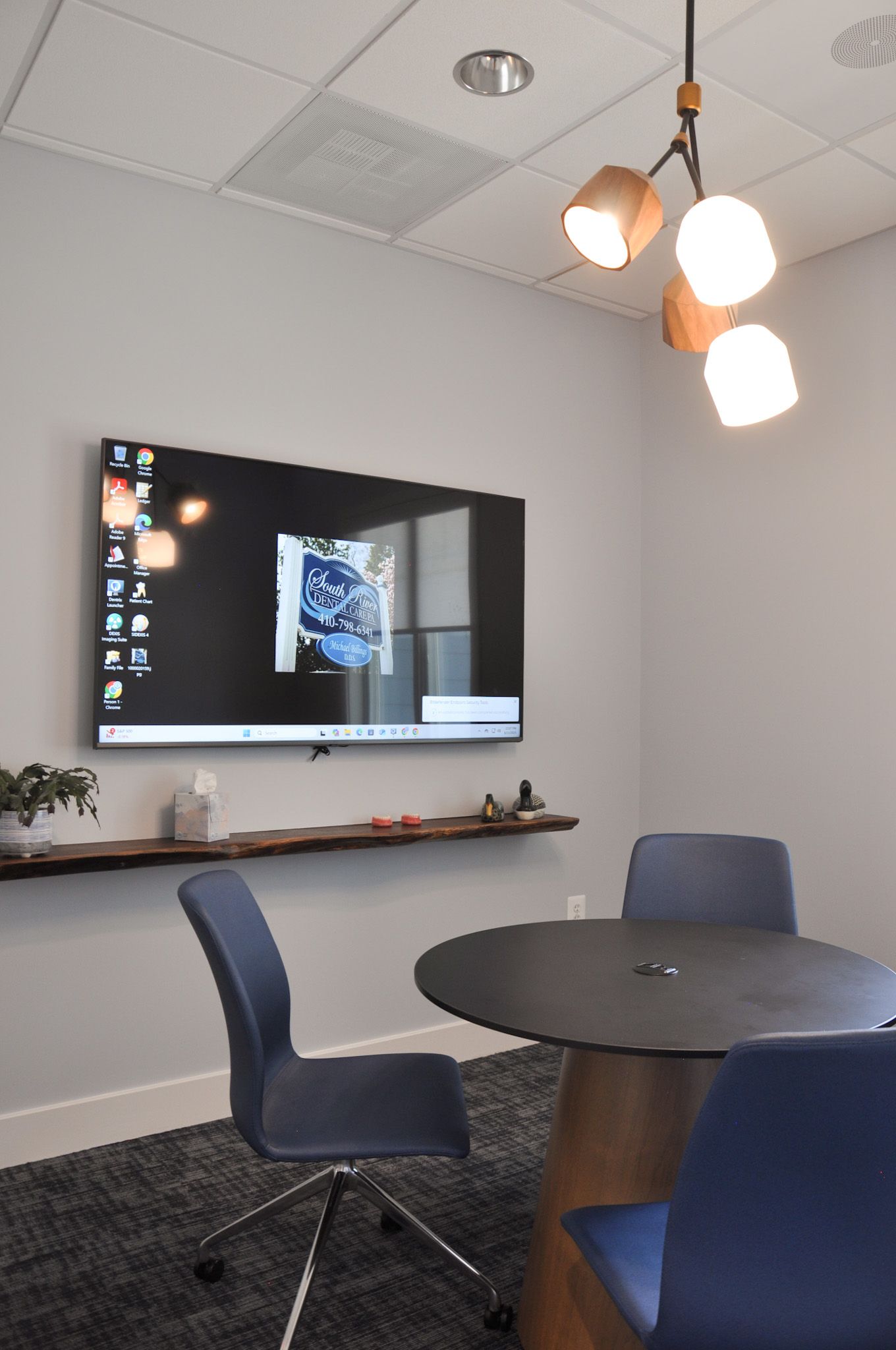 Conference room with a large screen, round table, blue chairs, and a unique light fixture.