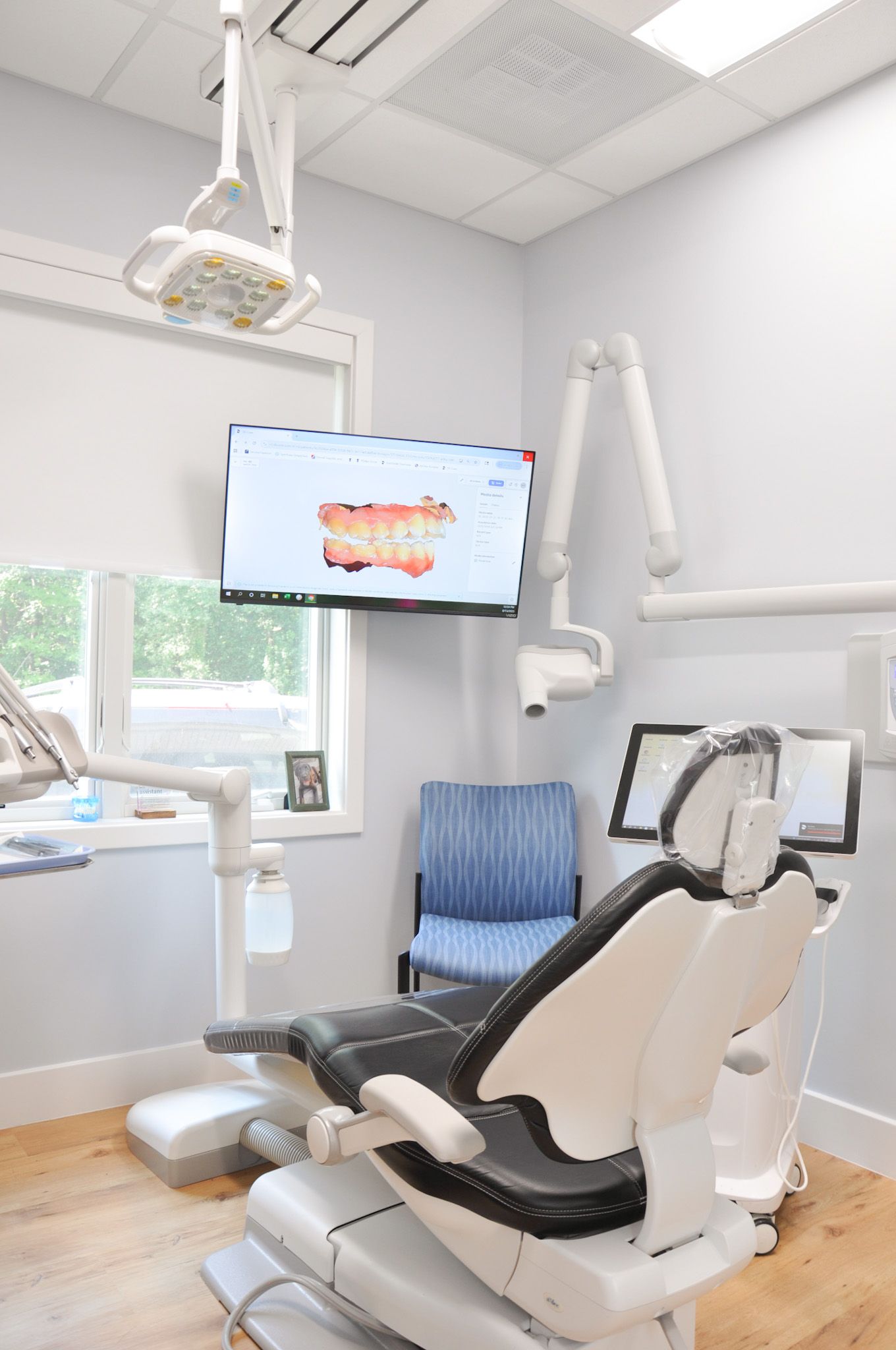 Dental office with chair, monitors, and equipment; light blue walls, wooden floor.