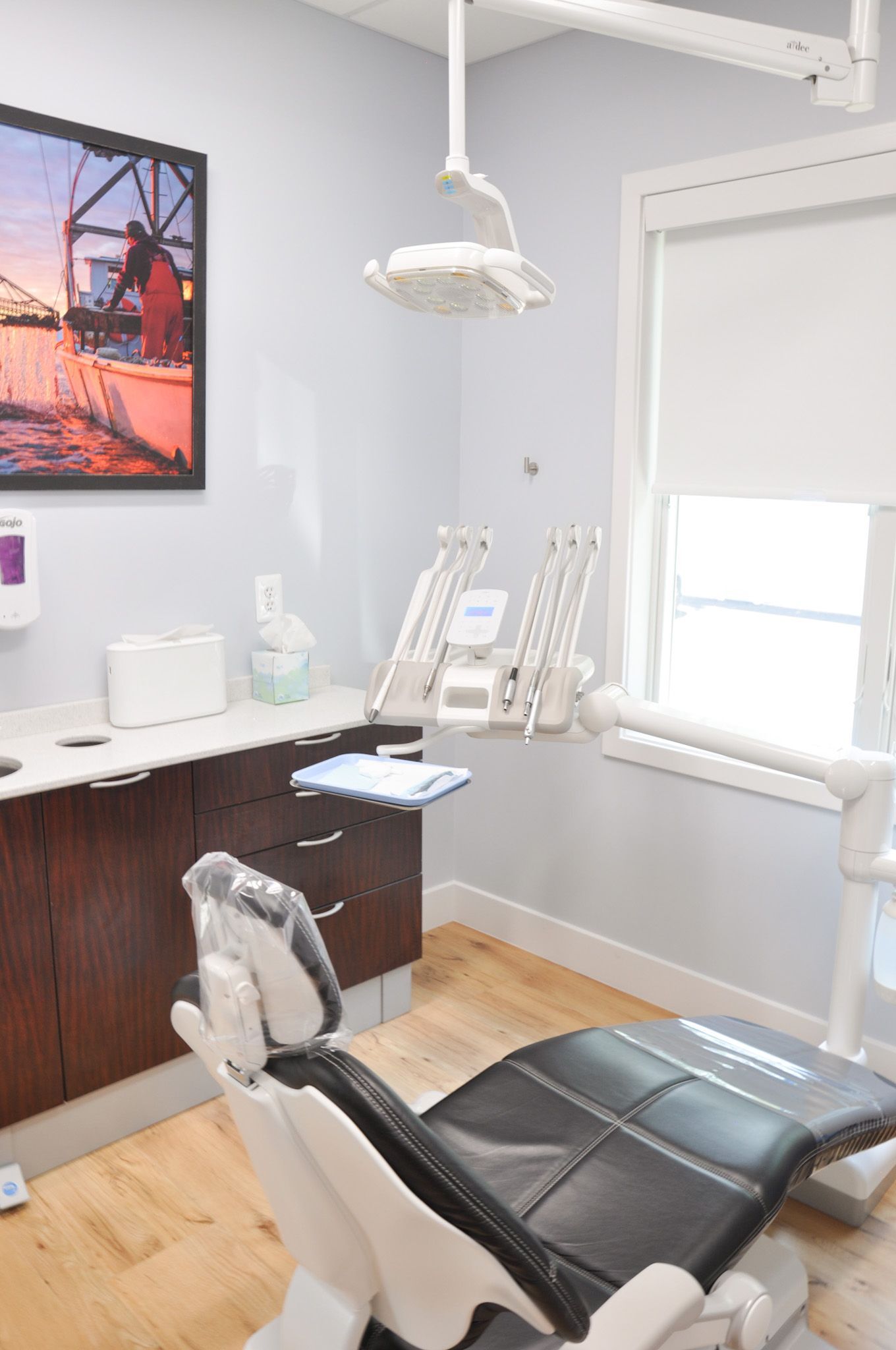 Dental office interior with dental chair, equipment, and a window.