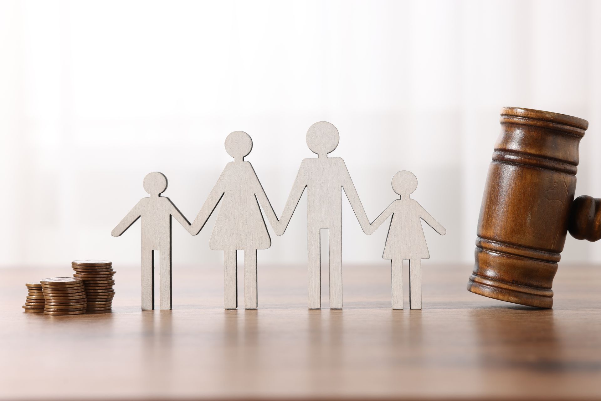 Wooden family figures, coins, and gavel on a table, symbolizing family law or financial decisions.