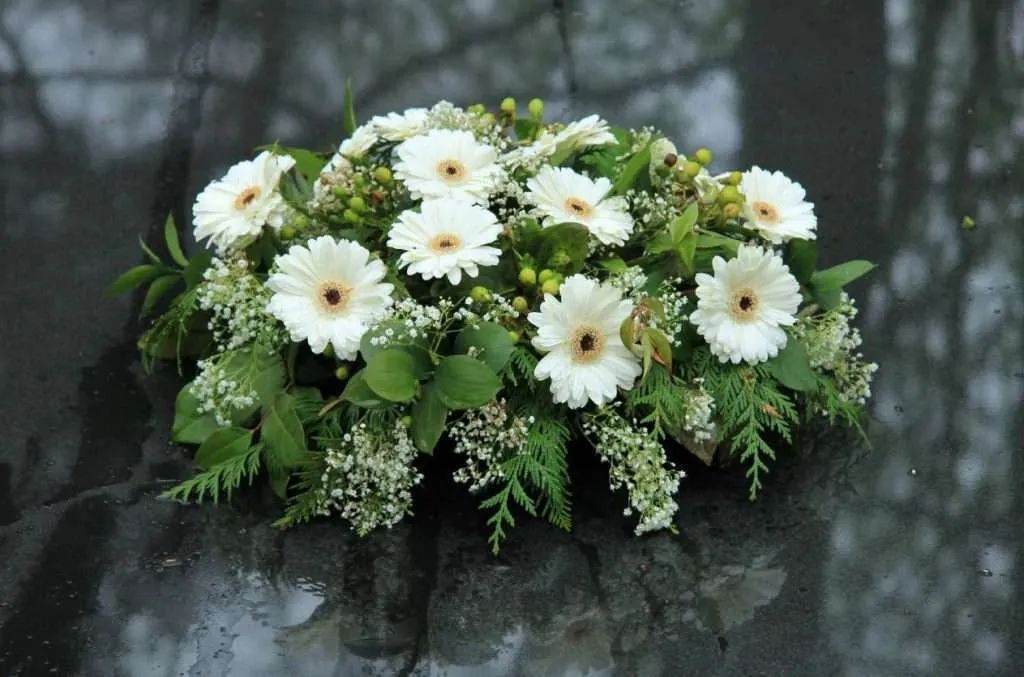 White Funeral Flower Arrangement With Daisies And Greenery Resting On Dark Surface Outdoors