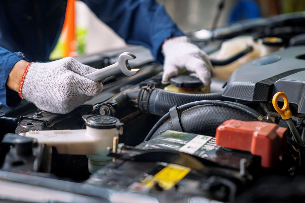 Le mani guantate di un meccanico che usano una chiave inglese sul motore di un’auto in un’officina