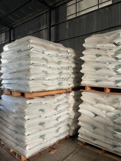 Montones de sacos blancos apilados sobre palés de madera dentro de un almacén.