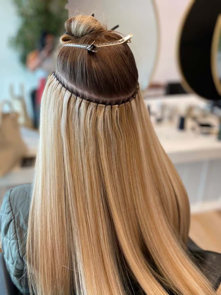 A woman with long blonde hair is sitting in a chair with her hair in a bun.