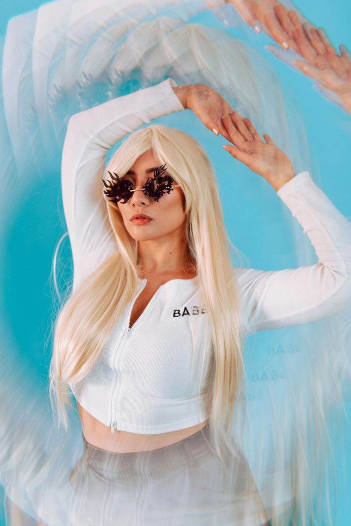 A woman with blonde hair and sunglasses is standing in front of a blue background.