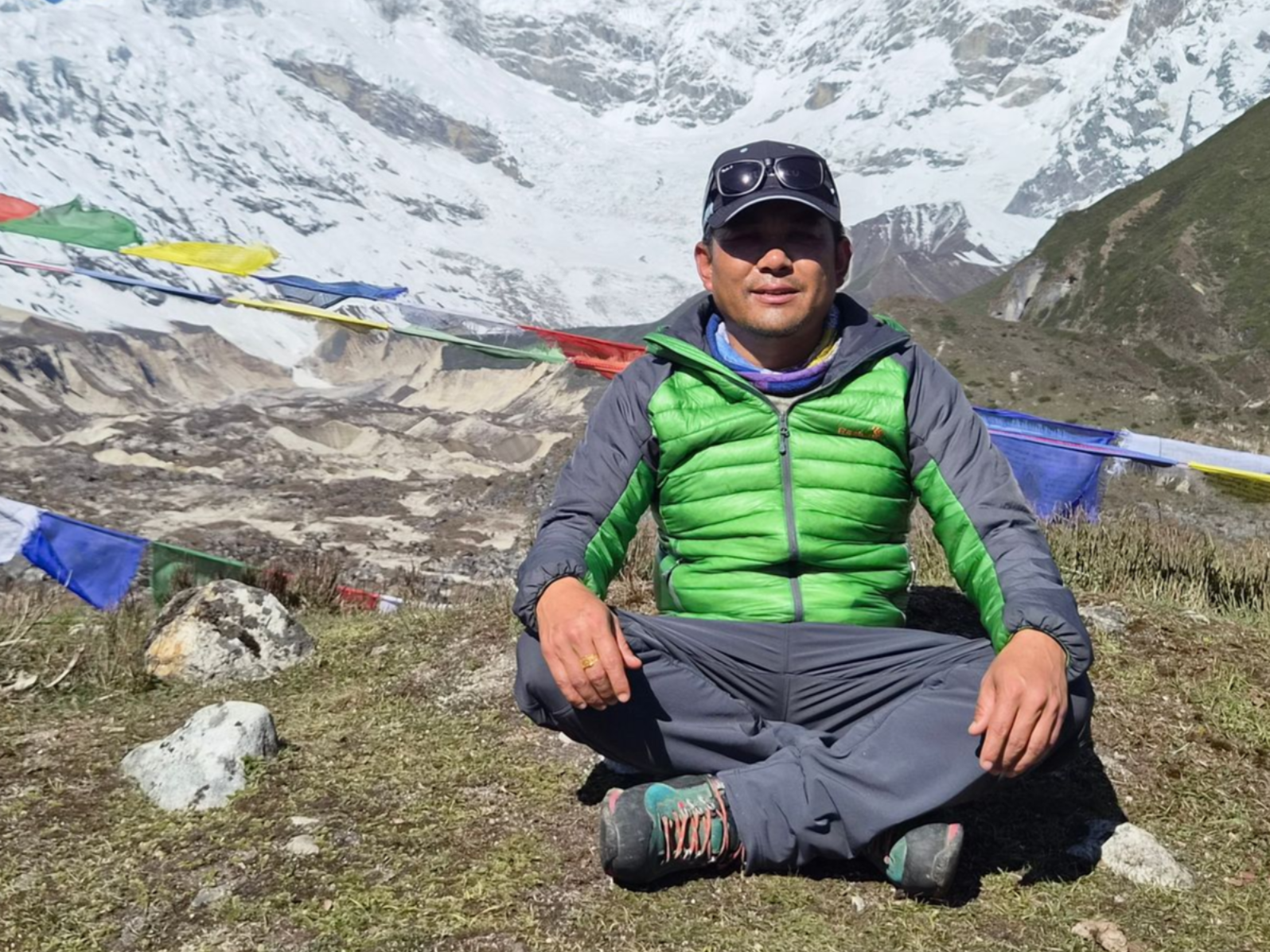 Trekking guide sitting at high altitude camp with prayer flags and snow-covered mountains in Annapurna region Nepal