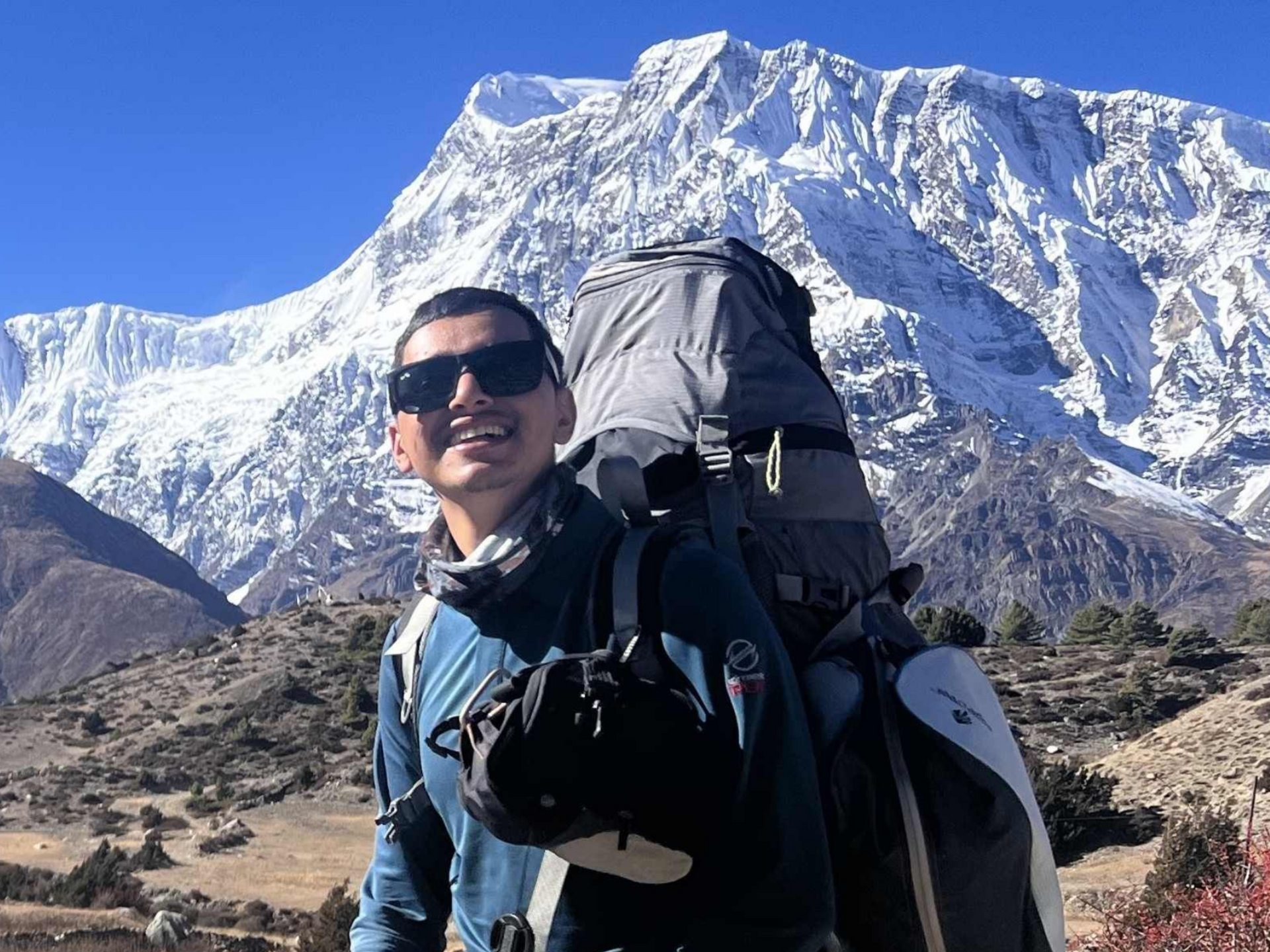 Licensed trekking guide with backpack and sunglasses in front of snow-capped Himalayan peaks, Nepal