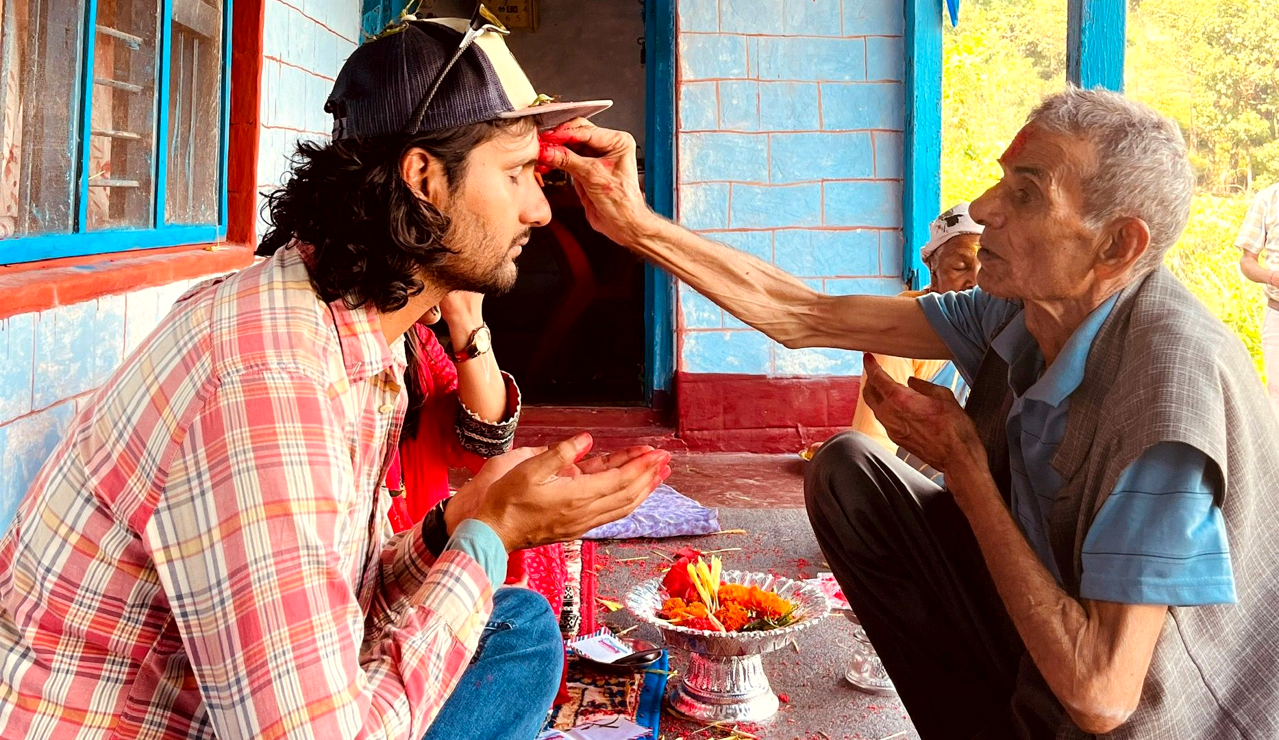 Elderly man giving red tika and Dashain blessings to a young man receiving them with open hands