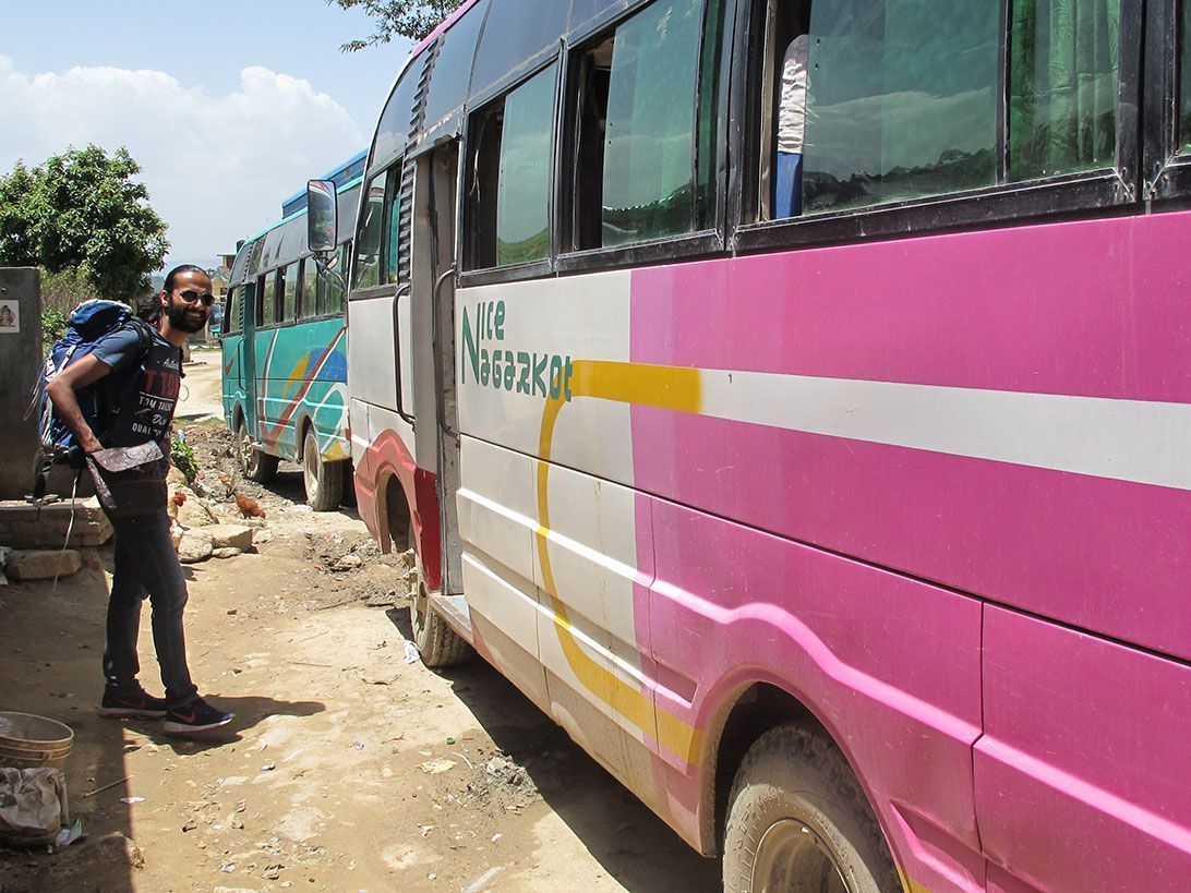 Traveler with a backpack next to a local bus, ready for transport from Kathmandu to Pokhara in Nepal.