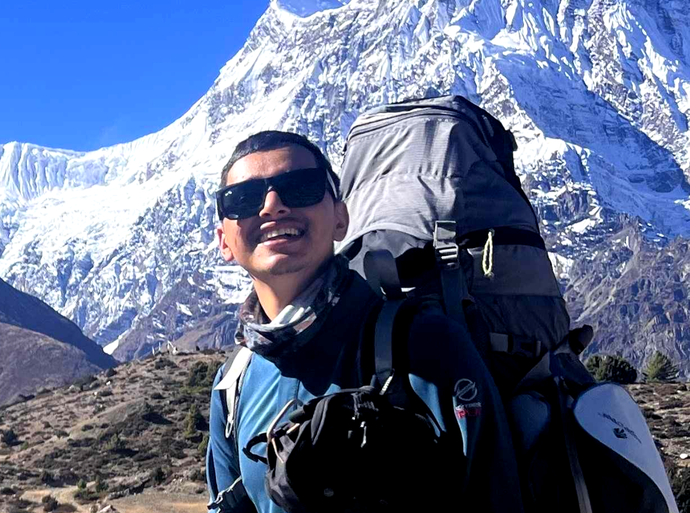 Licensed trekking guide with backpack and sunglasses in front of snow-capped Himalayan peaks, Nepal