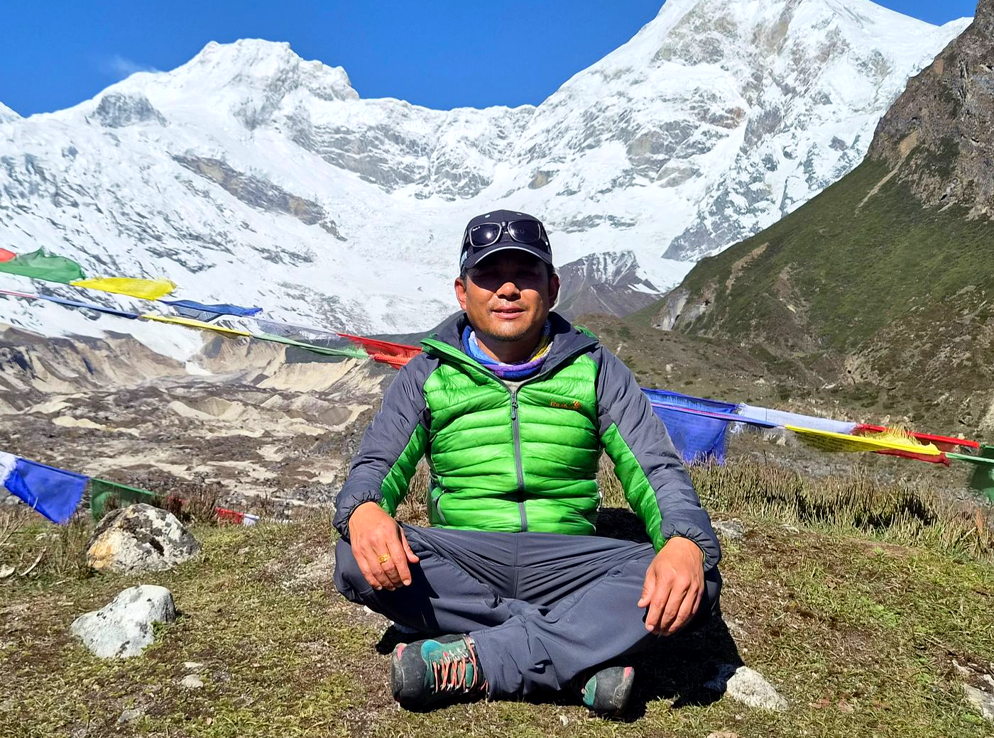 Trekking guide sitting at high altitude camp with prayer flags and snow-covered mountains in Annapurna region Nepal
