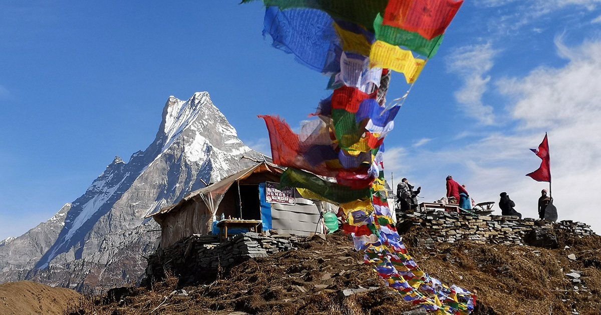 Colorful prayer flags flutter near a rustic shelter on the Mardi Himal trek, with Machhapuchare (6,993 m) towering behind.