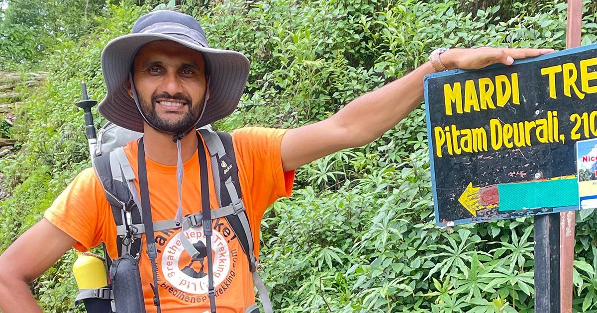 Trekking guide standing next to a Mardi Himal Trek sign, pointing towards the trailhead while surrounded by lush greenery.