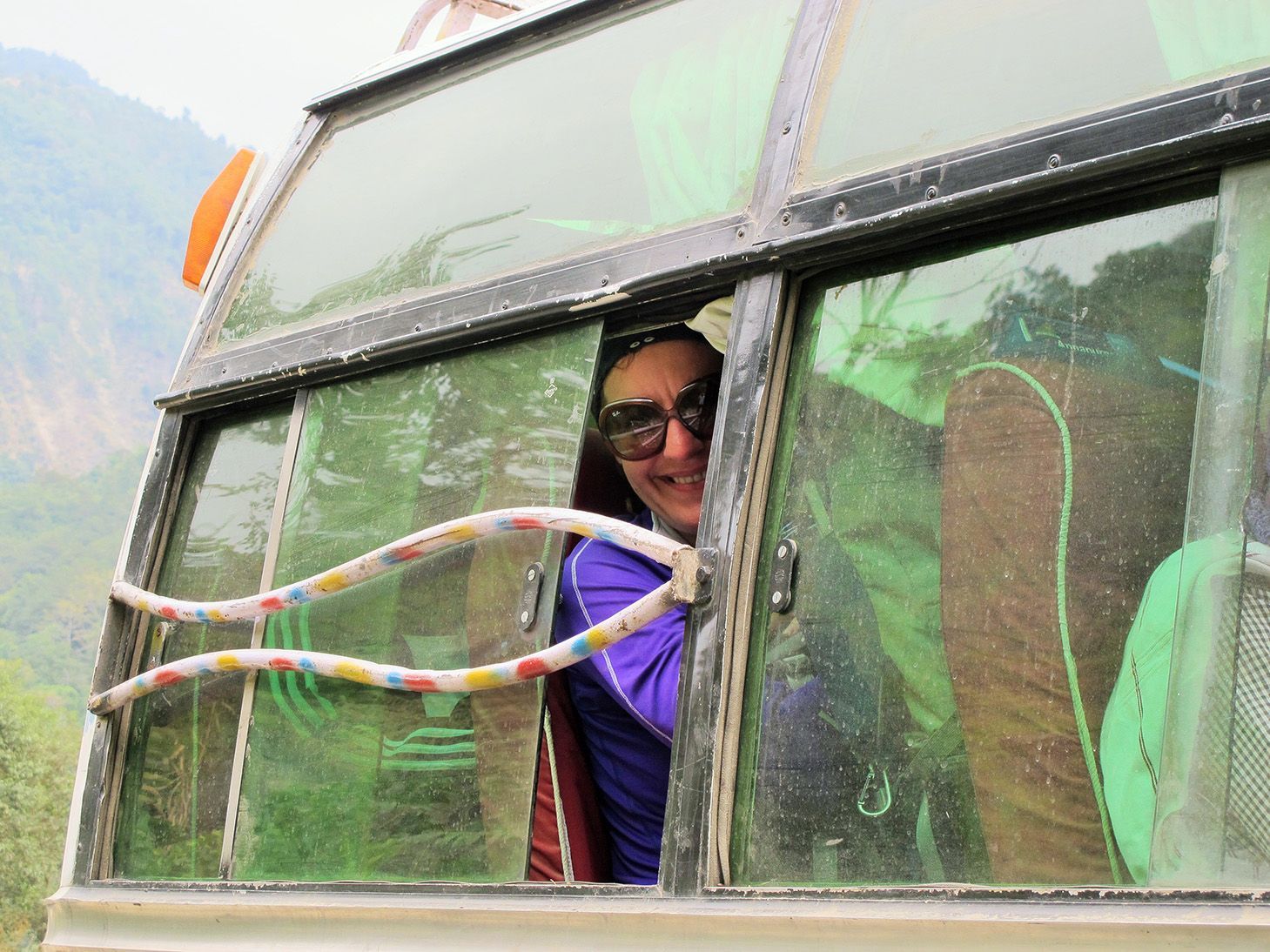A cheerful tourist in Nepal smiling from the window of a local bus, highlighting transportation options to Pokhara.