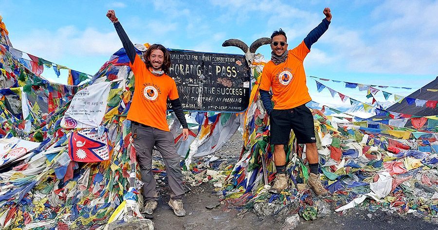 Two trekkers celebrate at Thorong La Pass (5,416 m) with colorful prayer flags behind them, showcasing their achievement.