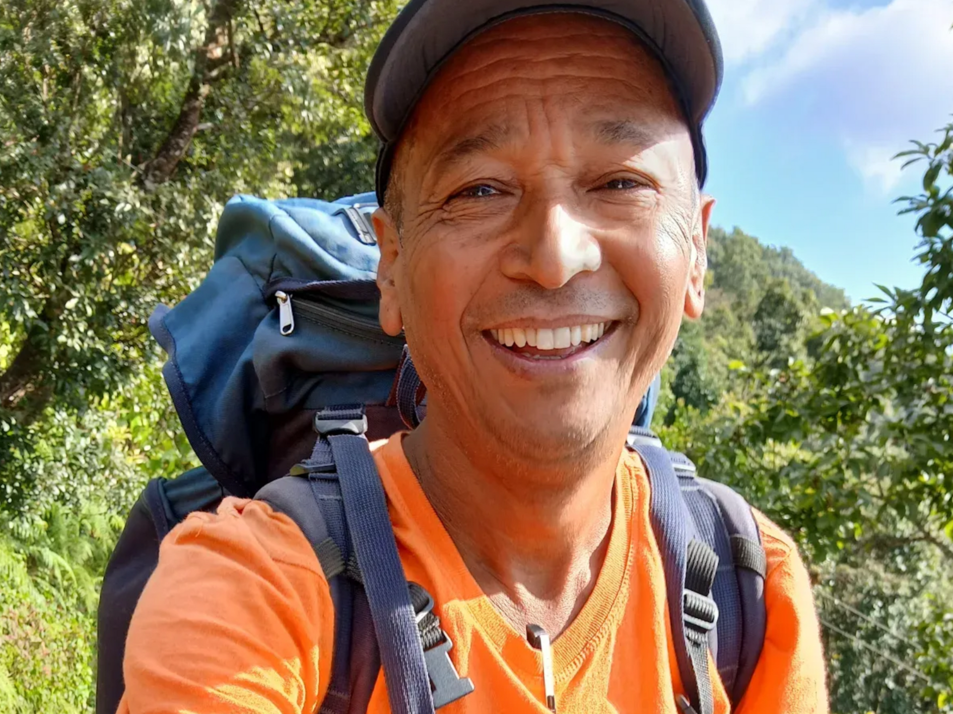 Smiling local trekking guide in orange jacket on a mountain trail in Nepal