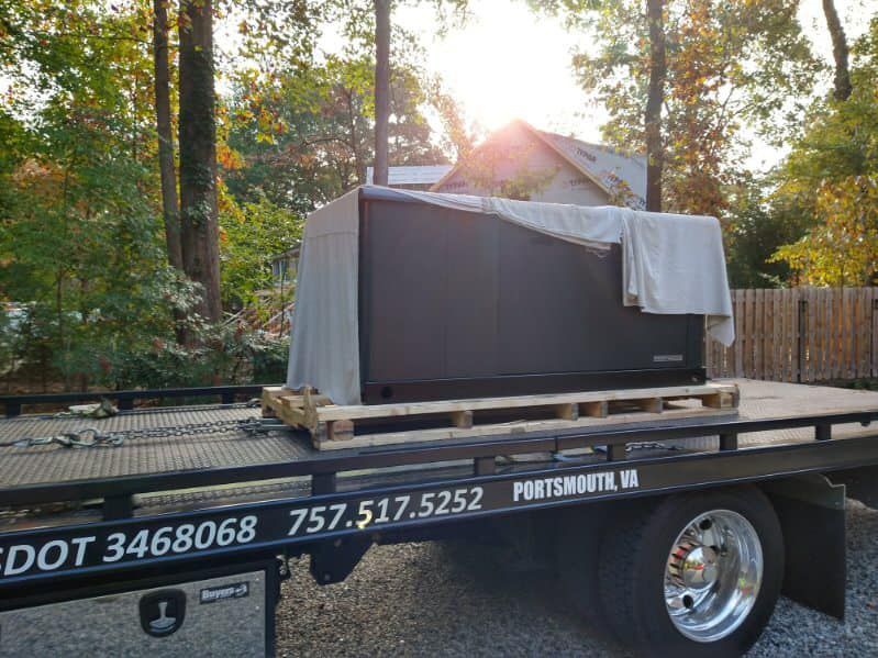 Covered appliance on a flatbed tow truck in a wooded driveway at sunset.