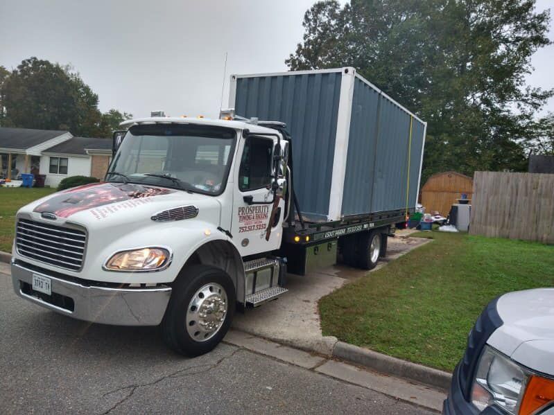 White flatbed truck carrying a blue shipping container parked on a suburban street