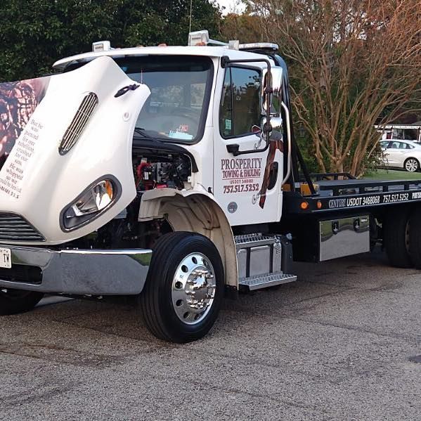 Tow truck with raised white cab hood parked on a street, showing engine area and flatbed.