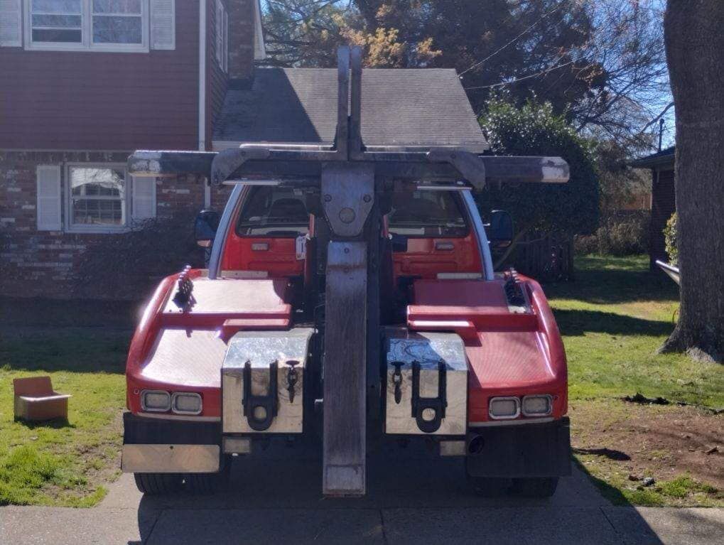 Red utility vehicle with a front-mounted plow parked in a driveway beside a house.