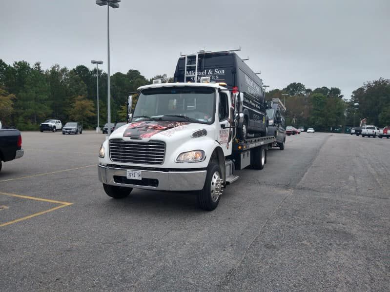 White semi-truck hauling a black dump trailer in a parking lot under overcast skies