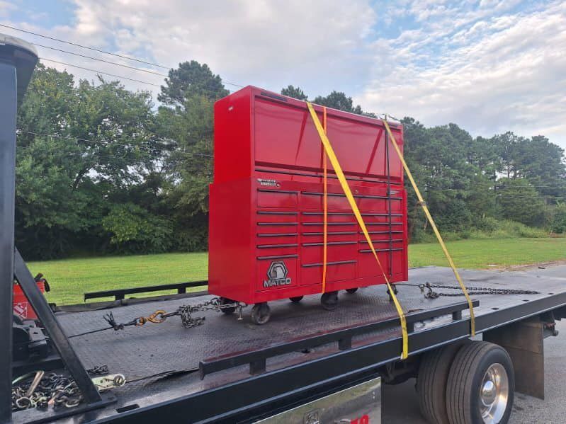Red tool cabinet strapped with yellow tie-downs on a flatbed trailer outdoors