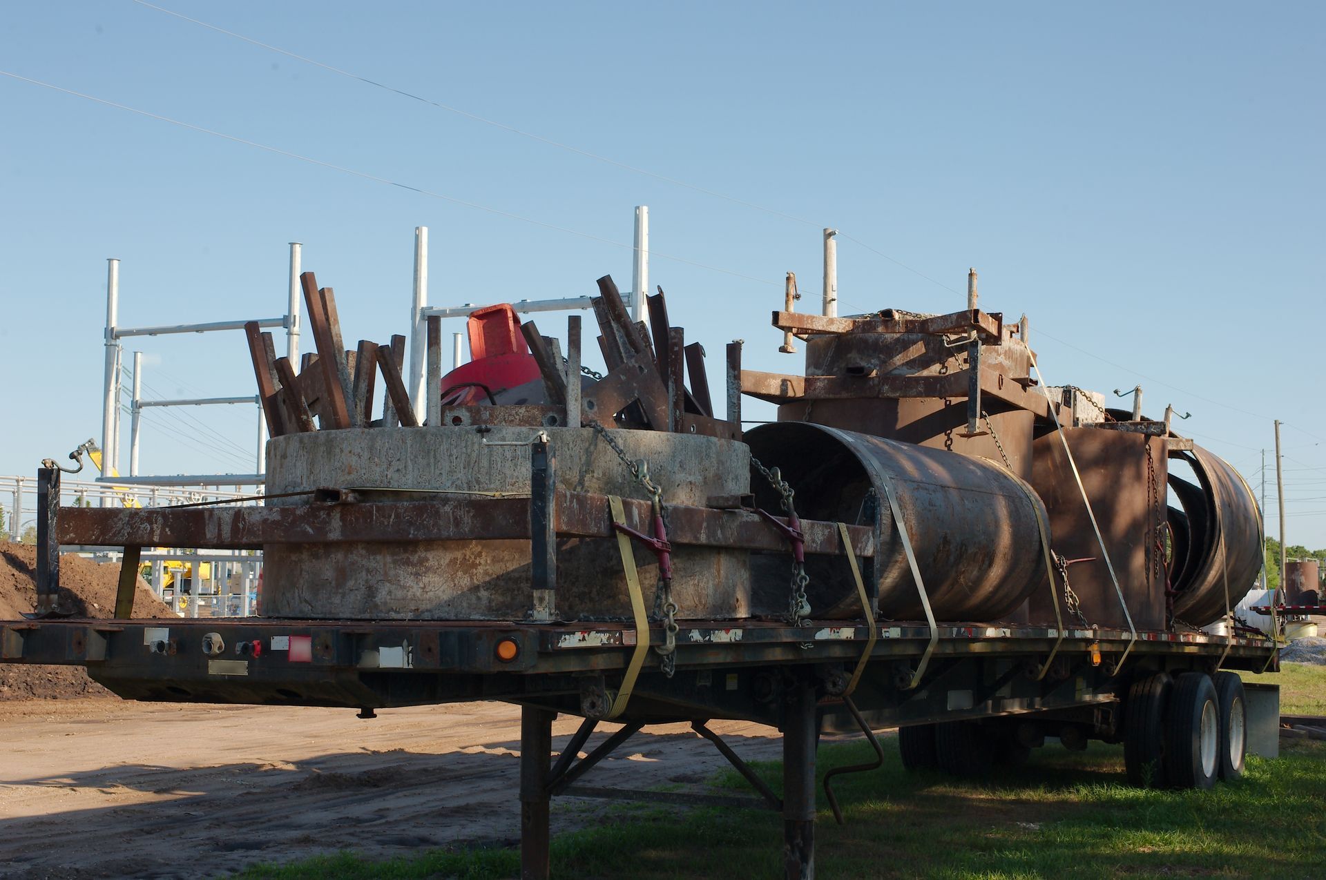 Rusty industrial trailer with large metal tanks and scrap, parked on grass under a clear sky.