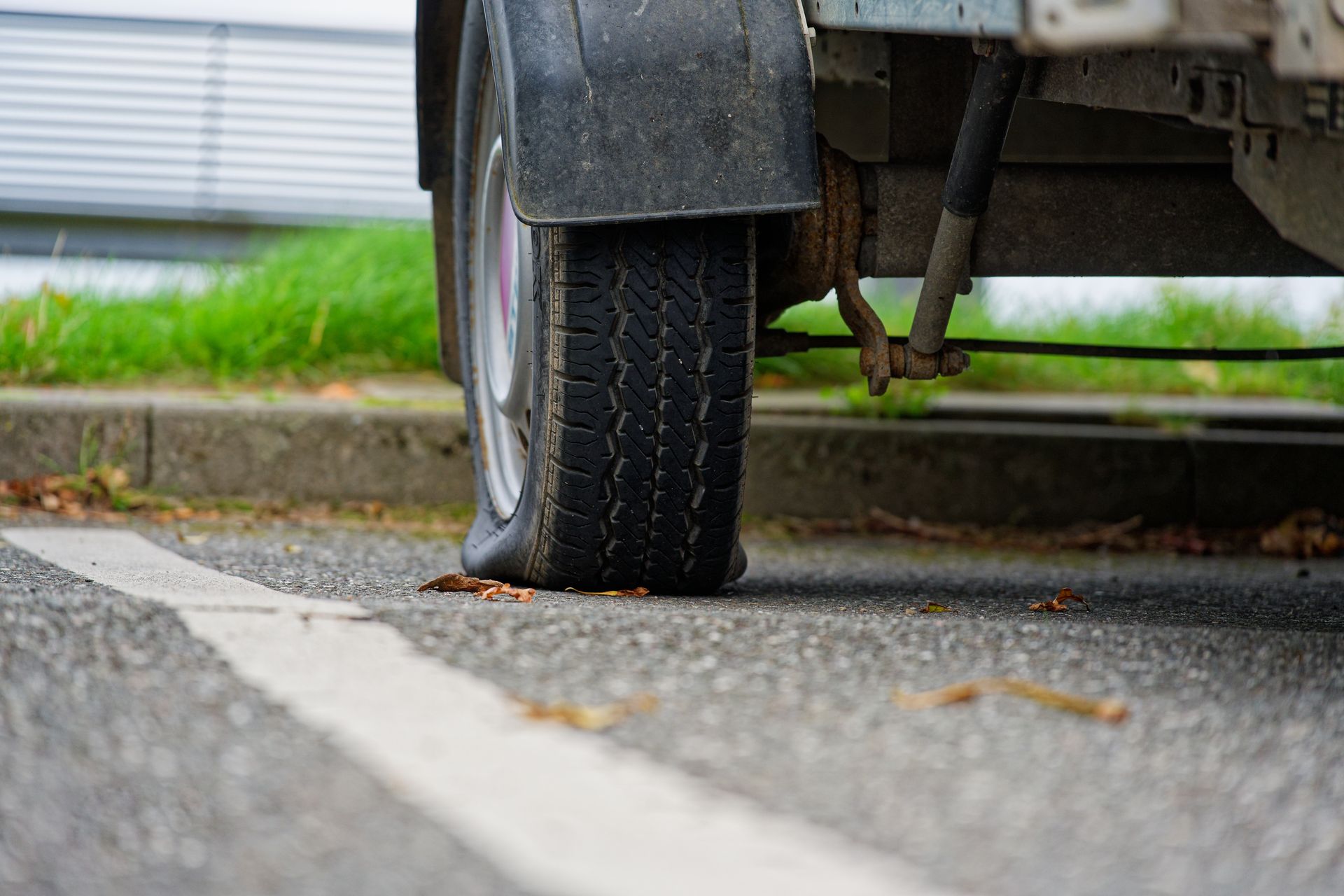 Flat tire on a vehicle parked at the curb, with the wheel resting on the pavement.