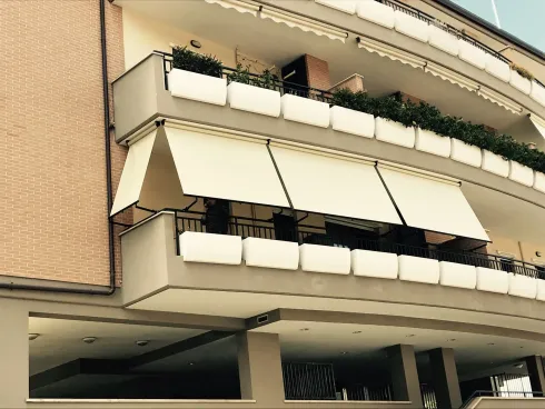 Balconi di un condominio con tende da sole bianche e piante in vaso su una facciata beige