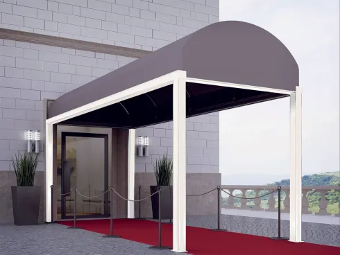 Ingresso moderno dell'edificio con tettoia grigia, colonne bianche, tappeto rosso e porte a vetri.