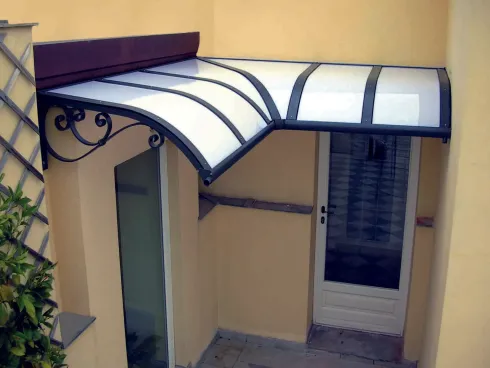 Ingresso coperto con tenda da sole ad arco bianca, mensole in ferro battuto e porta a vetri su una parete gialla