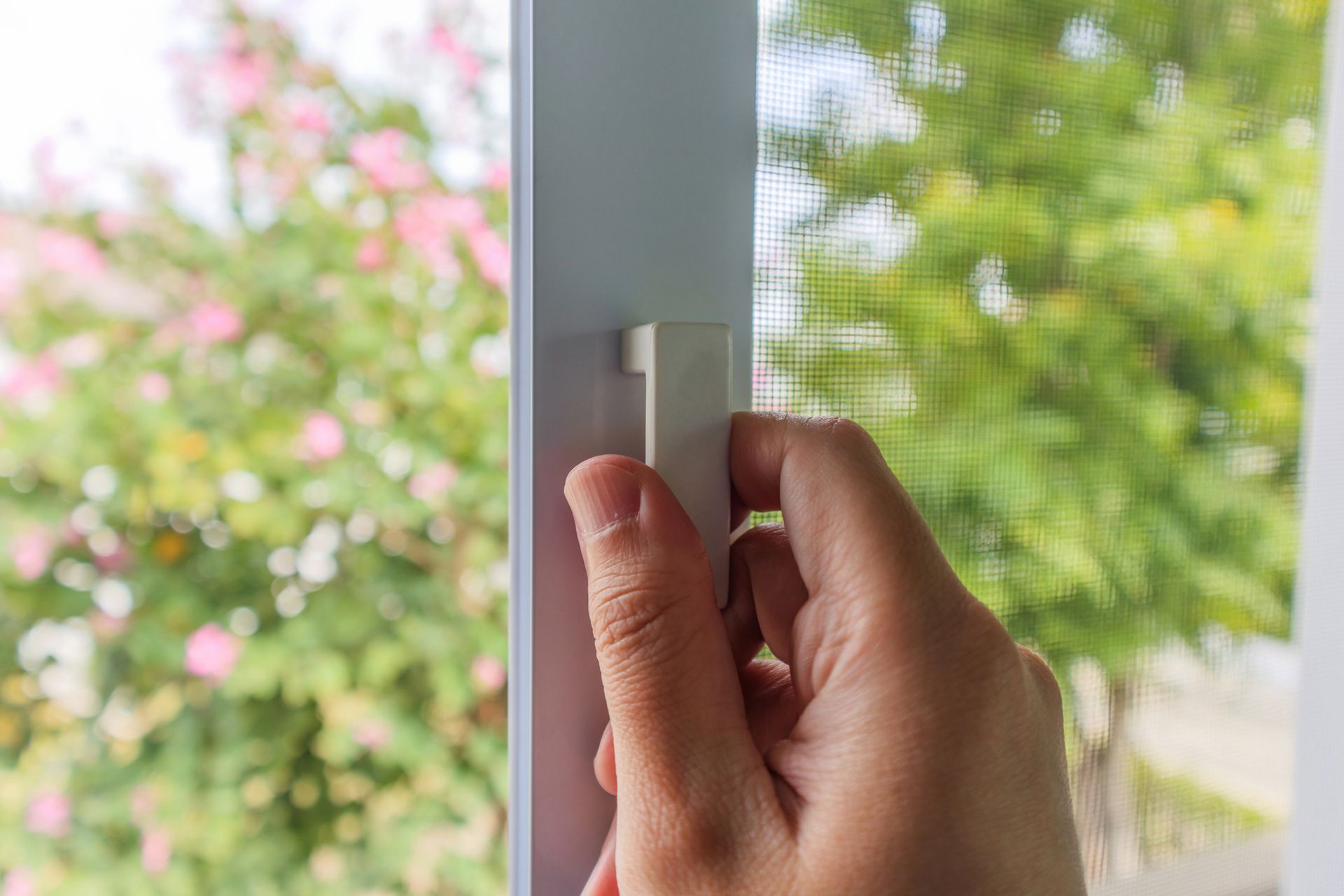 Una mano che gira un chiavistello bianco di una finestra accanto a una vista sfocata del giardino